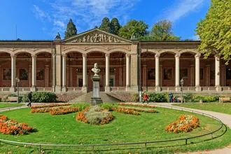 The long colonnaded front of the Trinkhalle with a fountain in the foreground