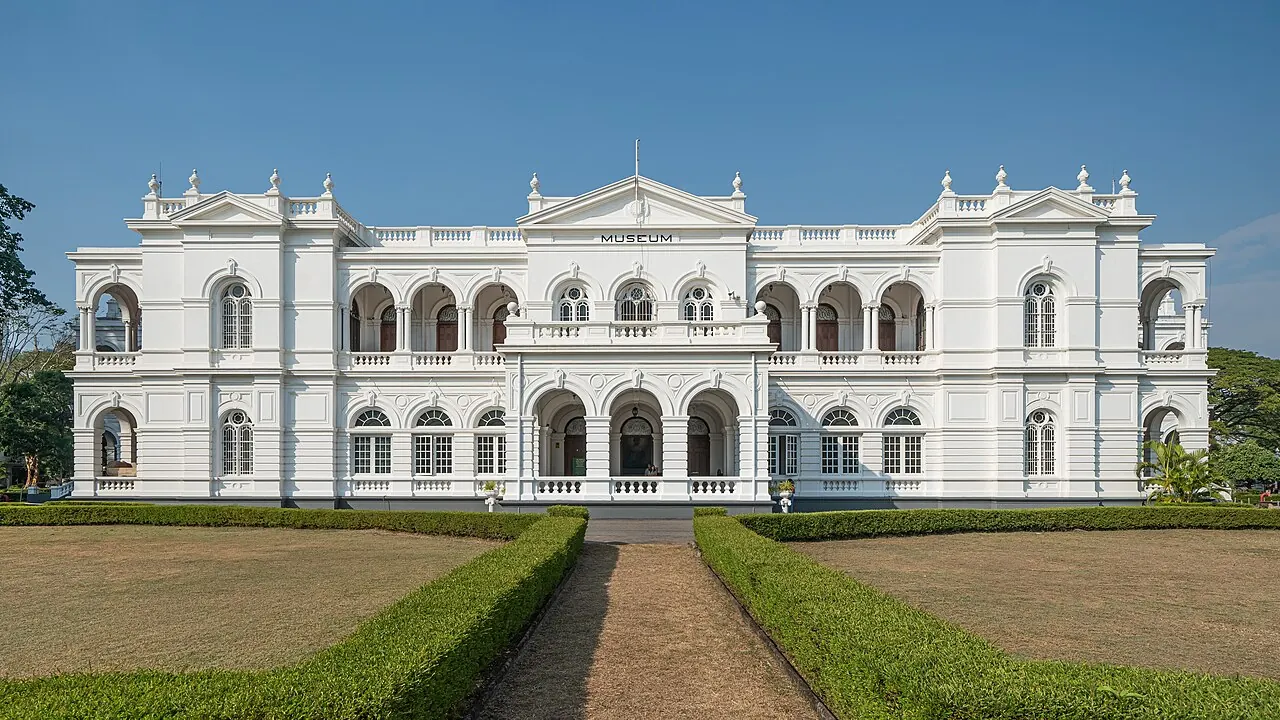 Die weiße Fassade des Nationalmuseums Colombo hinter einem Rasen und gestutzten Hecken