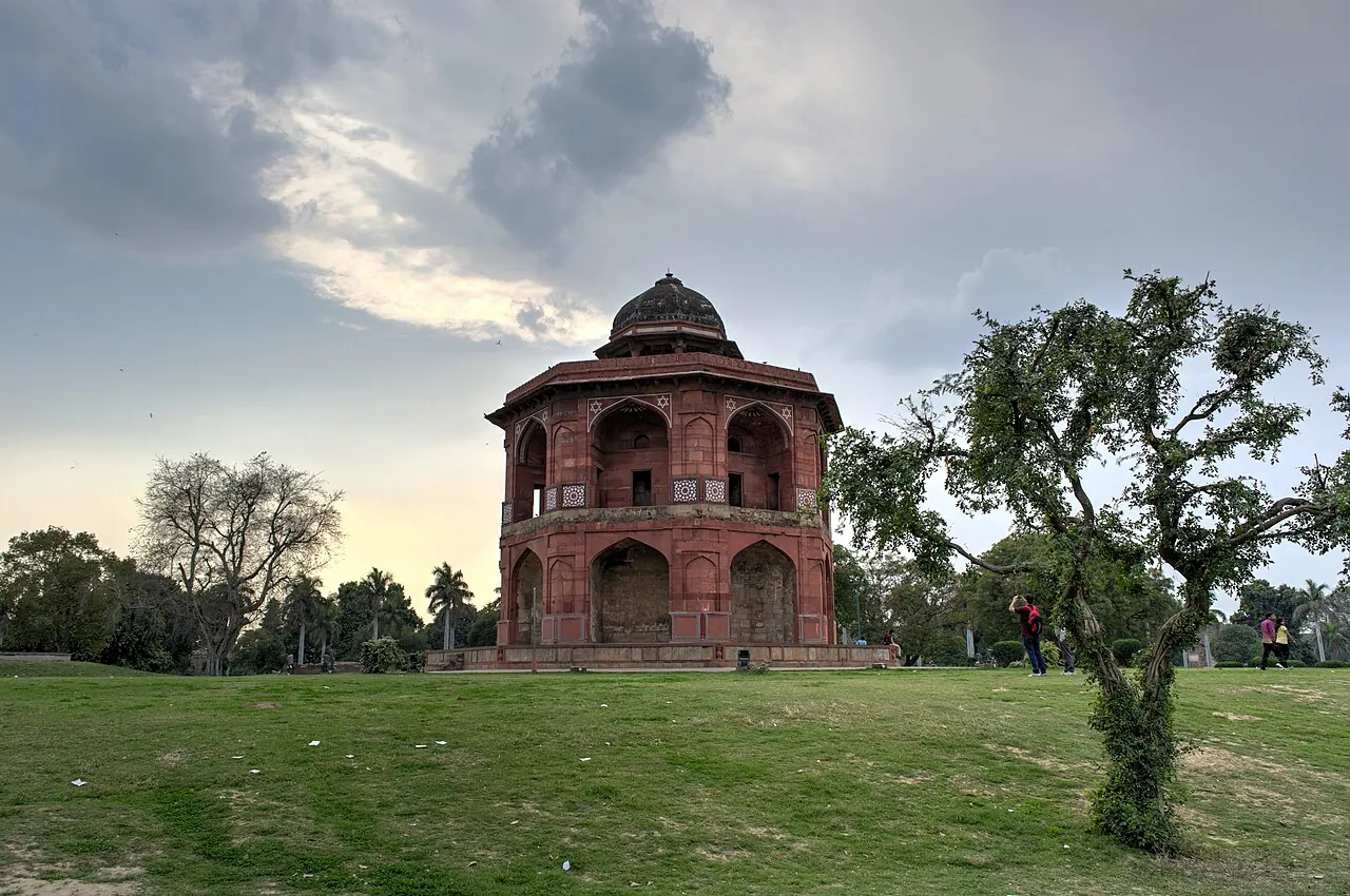 The red-sandstone Sher Mandal pavilion among grass and trees within Purana Qila