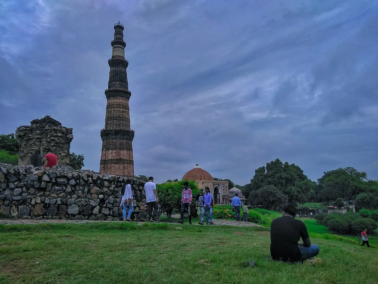 Qutb Minar rising in full above ruins and garden paths within the Mehrauli complex