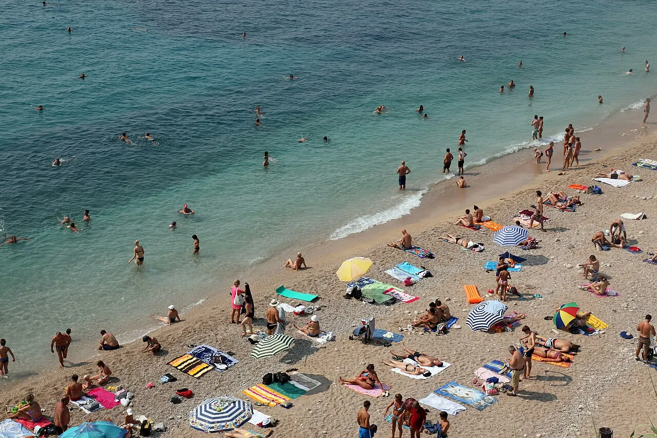 People on the pebble shore and in the water at Banje Beach in Dubrovnik's Ploce