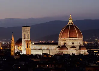 Florence Cathedral's illuminated dome and bell tower against the hillside at dusk