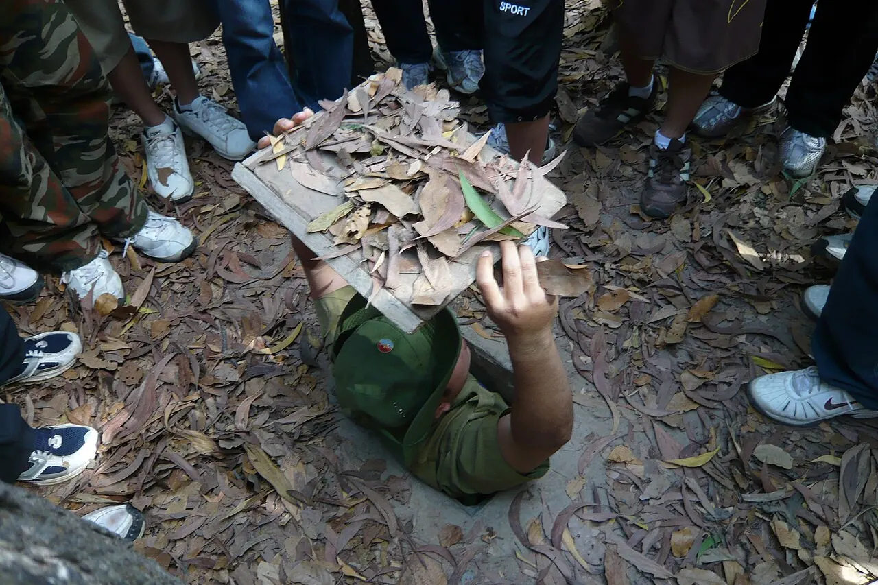 A visitor demonstrating the narrow camouflaged entrance to a Cu Chi tunnel
