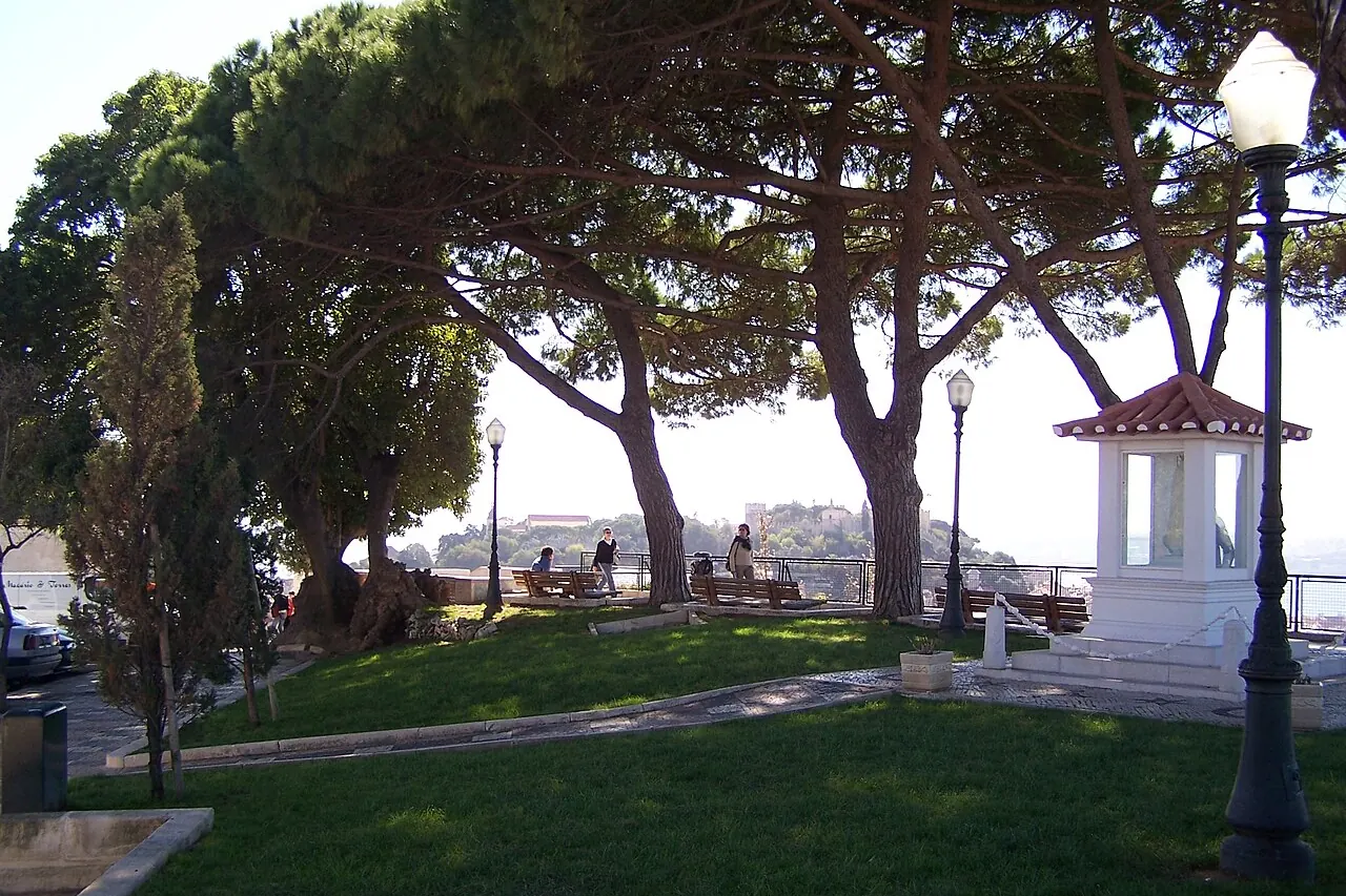The shaded viewpoint area at Senhora do Monte with Lisbon visible beyond the trees