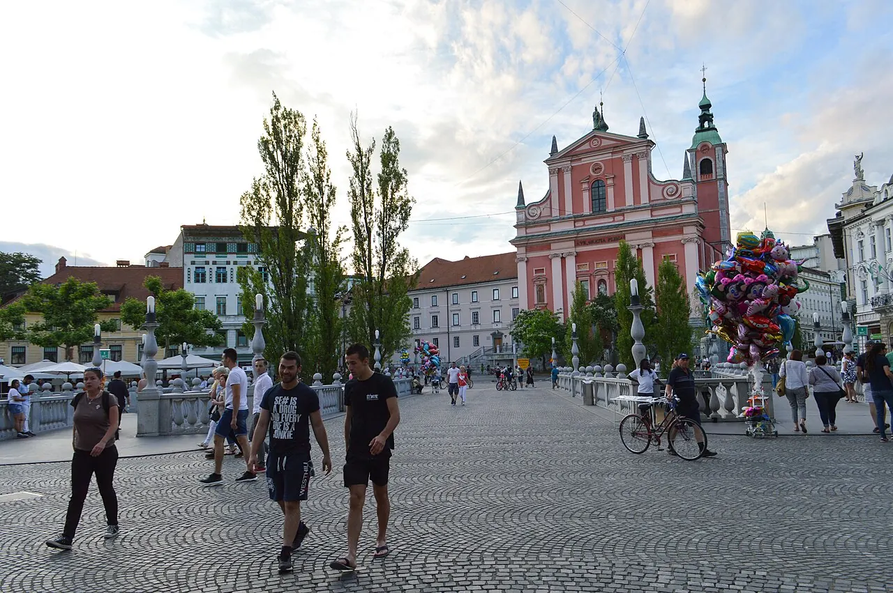 Pedestrians crossing Triple Bridge towards the pink Franciscan Church in Ljubljana