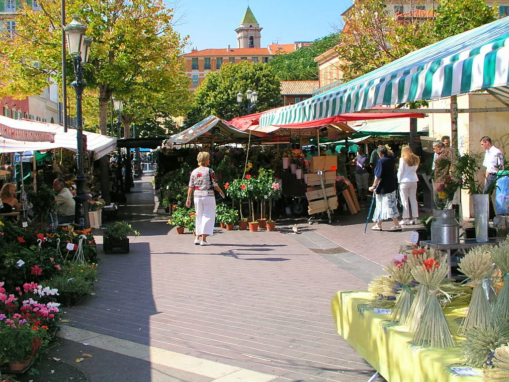 Shoppers walking between produce stalls and striped market awnings on Cours Saleya