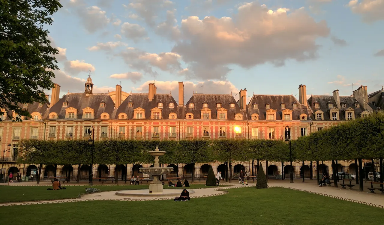 Lawns, a fountain and the arcaded brick buildings of Place des Vosges in Le Marais