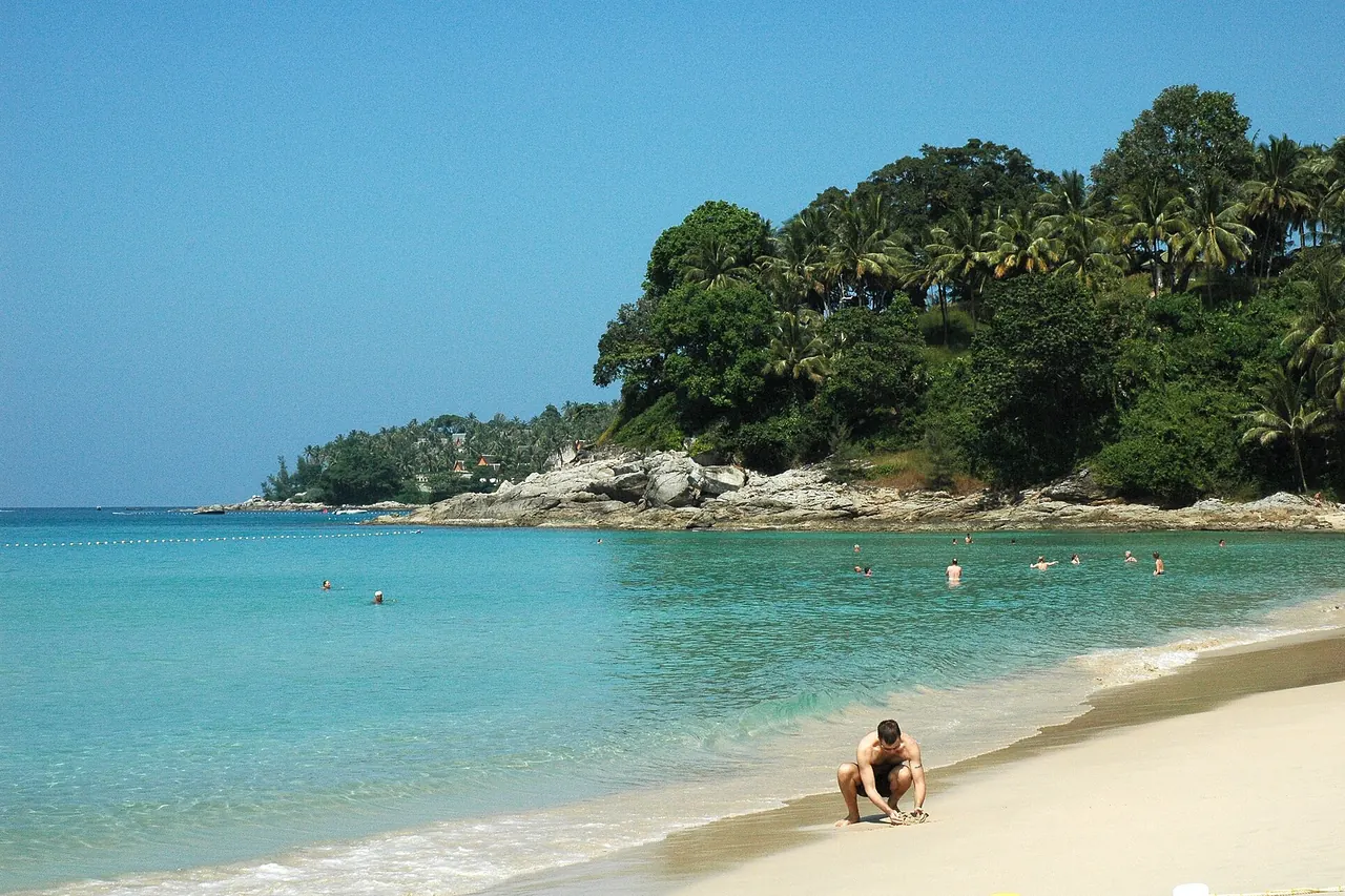 The pale sand, clear-looking water and wooded headland at Surin Beach