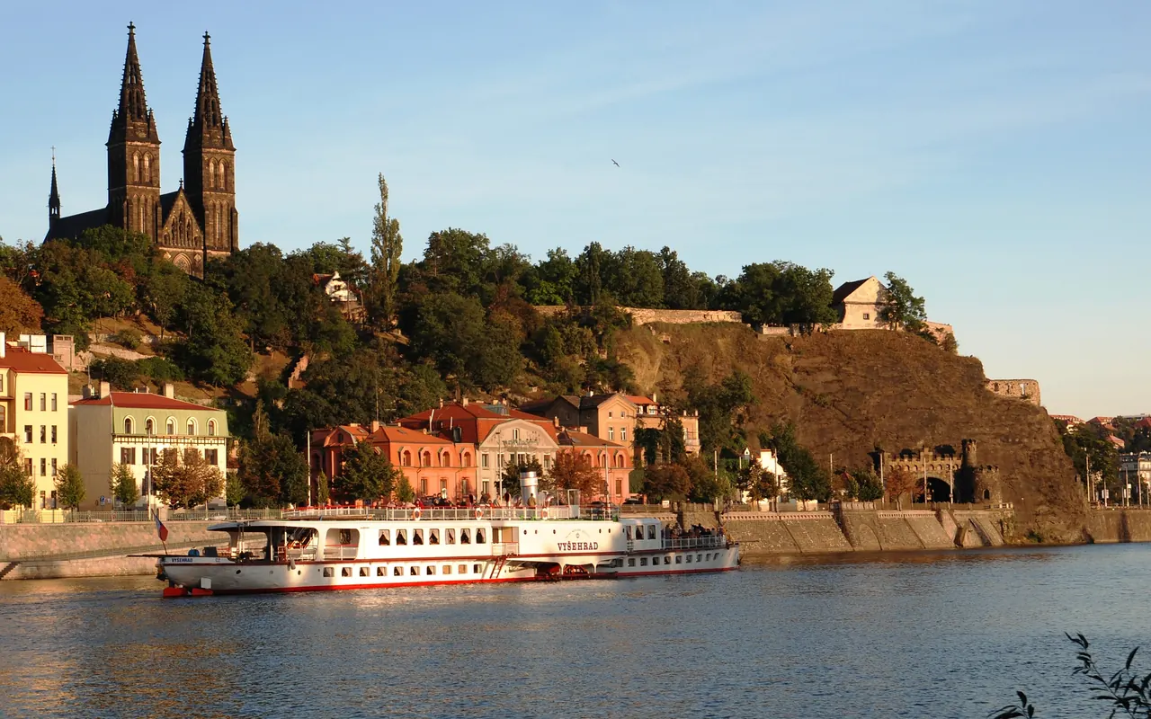 Vysehrad's walls and church towers above the river, with a passenger boat below