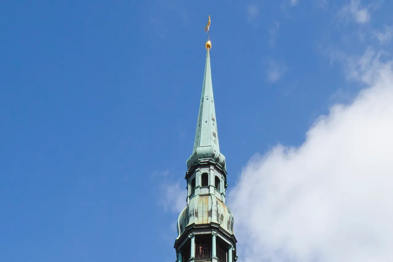 Upper tower and slender spire of St Peter's Church against the sky in Riga