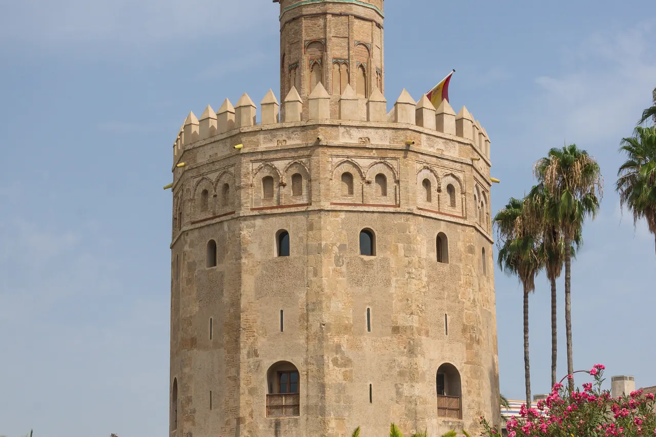 Stone exterior of the Torre del Oro with palm trees in Seville