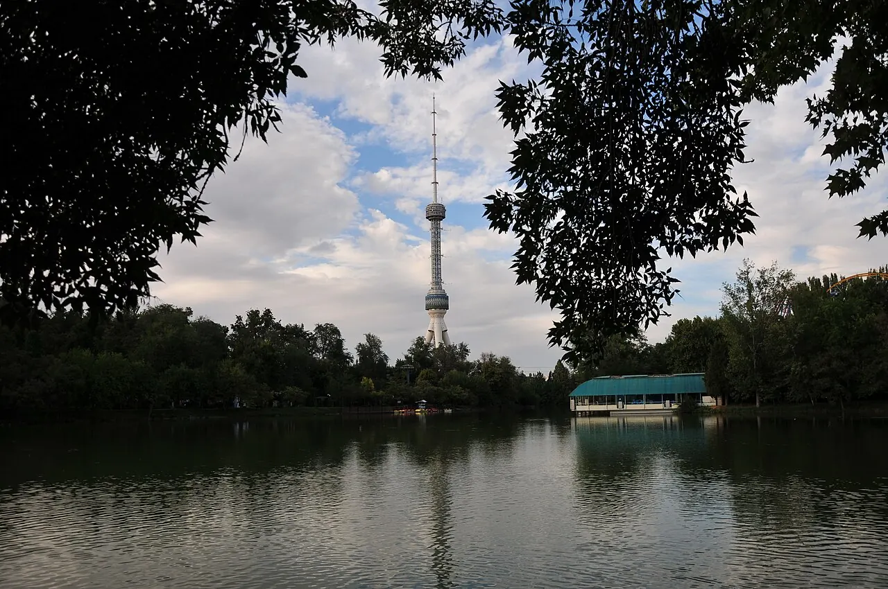 Tashkent TV Tower rising behind trees and a lake under a cloudy sky