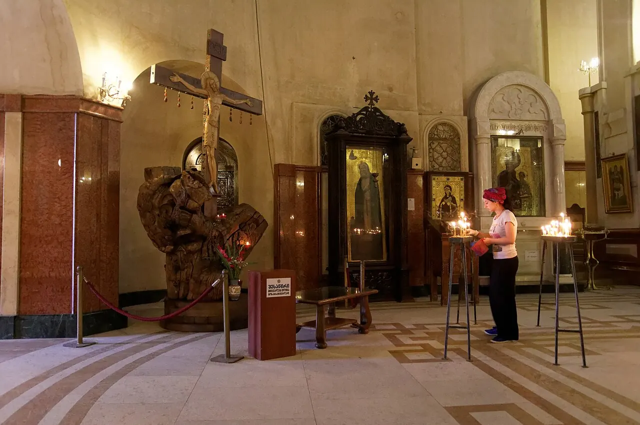 Icons, candles and stone arches inside Holy Trinity Cathedral in Tbilisi