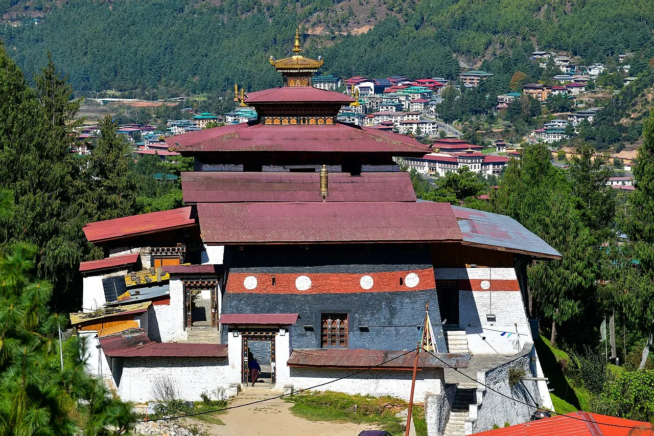 Dunkles Holz und weiße Mauern von Changangkha Lhakhang über Häusern an einem Hang in Thimphu