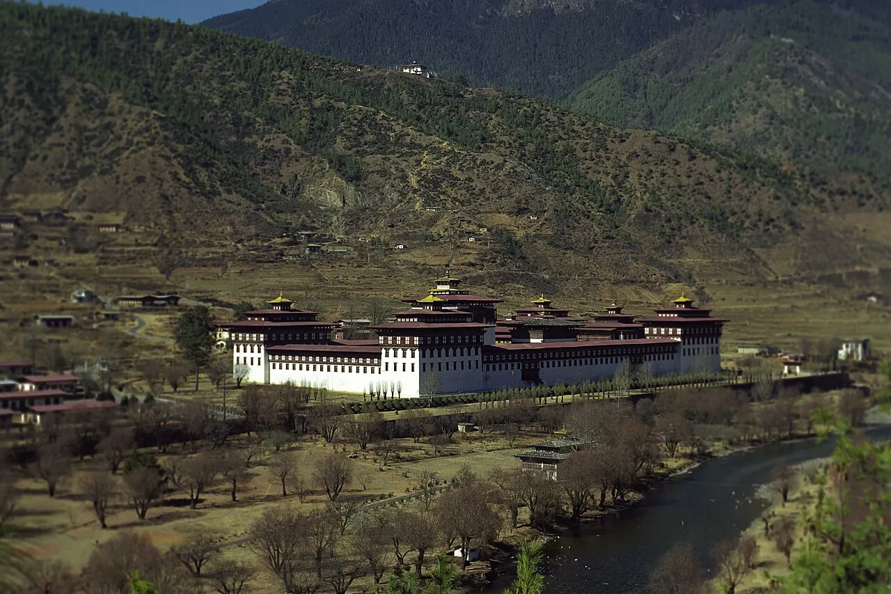 Der lange, weiß ummauerte Tashichho Dzong mit traditionellen Dächern unterhalb der Hügel von Thimphu