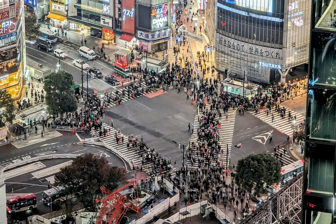 Pedestrians crossing the marked lanes at Shibuya with illuminated buildings behind