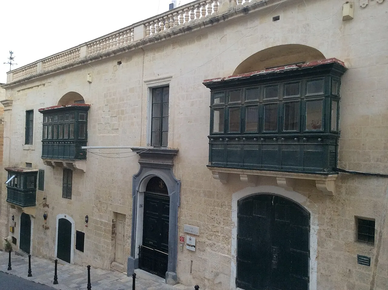 Casa Rocca Piccola’s stone facade, green balcony and entrances on Republic Street in Valletta