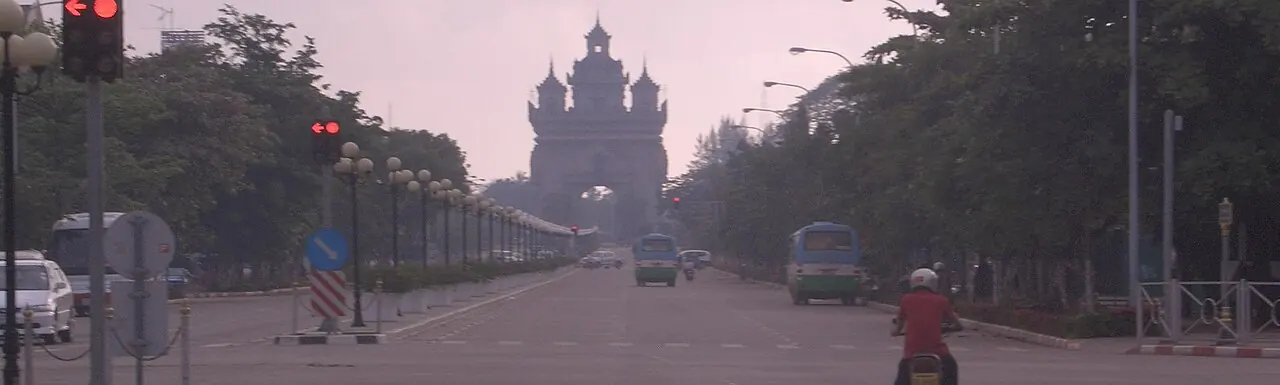 Patuxai seen along Lane Xang Avenue with trees and traffic in the foreground